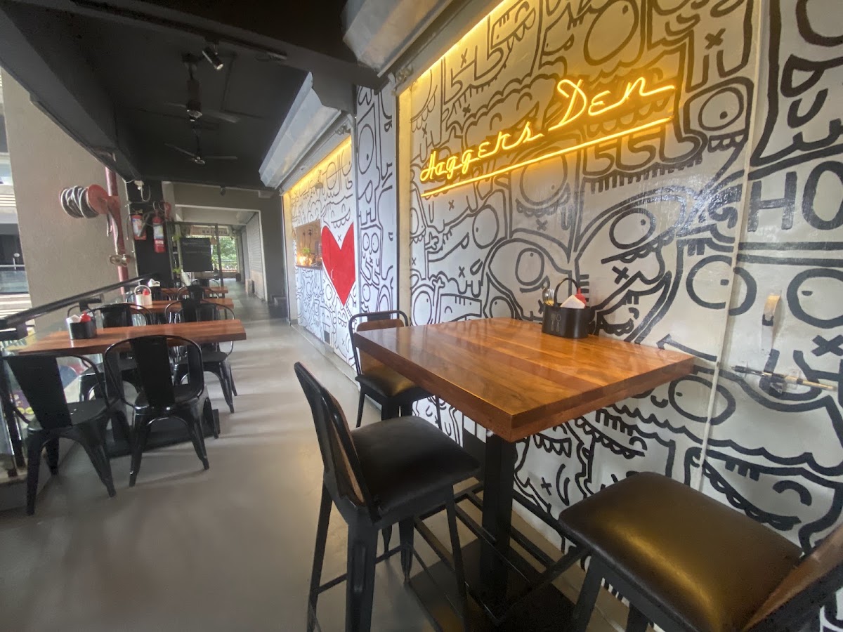 Inside Hogger's Den — doodle mural wall under the amber neon sign, with wood tables